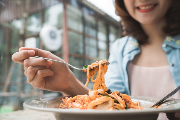 レストランやカフェでイタリアのシーフードスパゲッティのプレートを食べている美しい幸せなアジアの女性