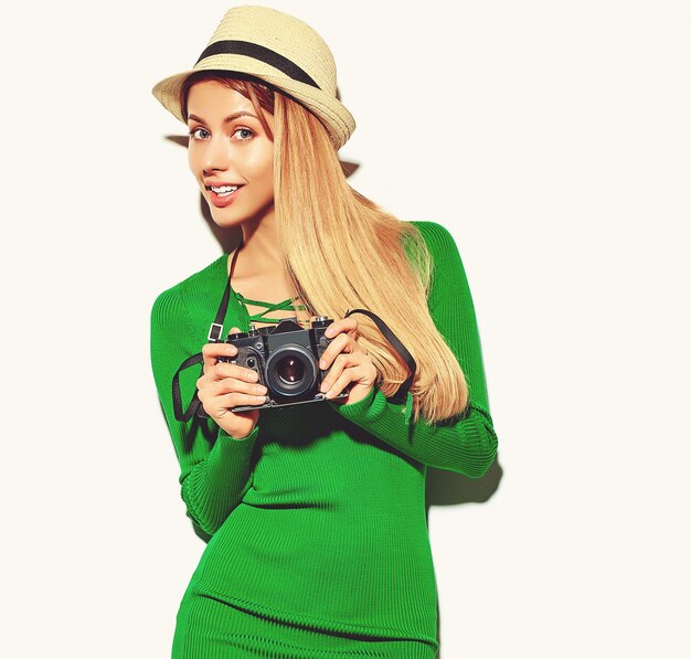 カジュアルな夏の緑のヒップスターの服で美しい幸せなかわいい金髪の女性の女の子は、レトロな写真用カメラを保持している写真を撮る