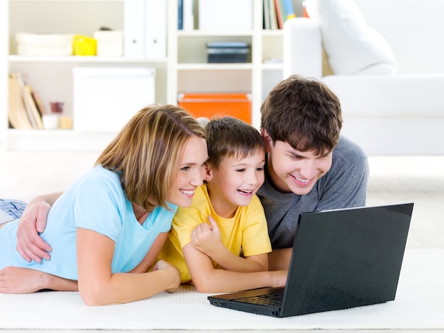 Beautiful happy family with child looking at laptop with cheerful smile - indoors