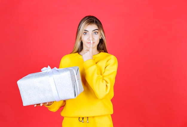 Beautiful happy girl holding gift box on red wall