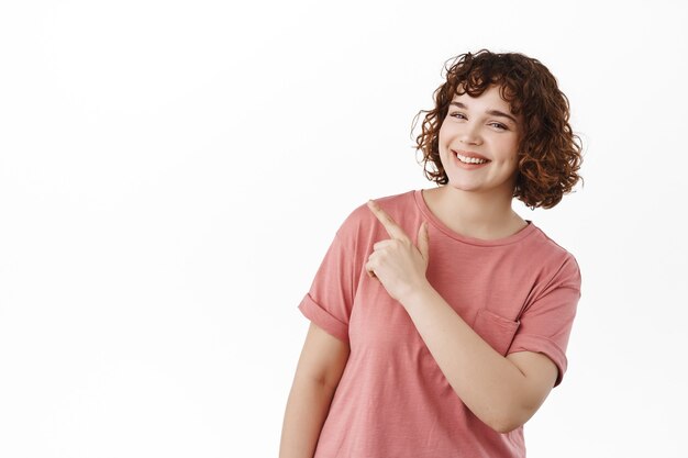 Beautiful happy girl, smiling white teeth, pointing at upper left corner and showing copy space on white