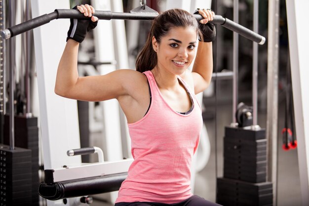 Beautiful happy girl wearing a sporty outfit and gloves exercising at the gym