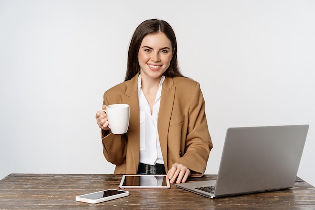 Beautiful happy office lady business woman drinking coffee at work sitting at table and smiling plea...