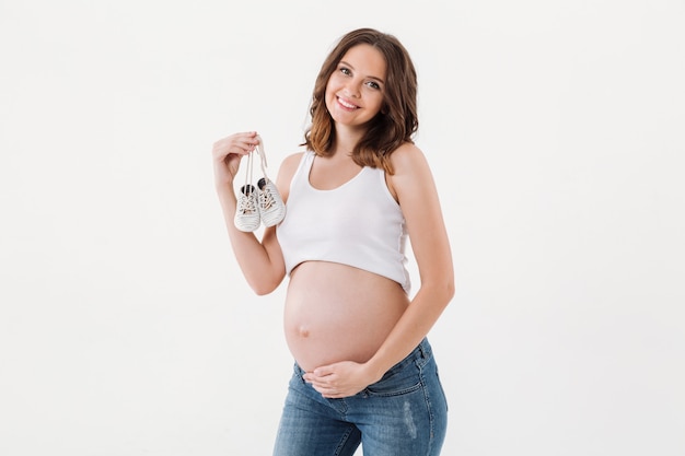 Beautiful happy pregnant woman holding little baby shoes.