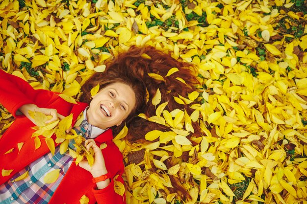 Beautiful happy woman laying in yellow autumn leaves.