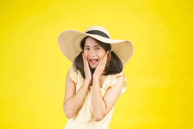 A beautiful, happy woman wearing a big hat showing cheerfulness on a yellow .