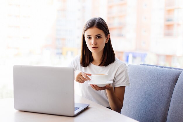 カフェバーでのコーヒーブレーク中にラップトップコンピューターで作業して美しい幸せな女