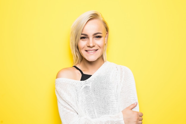 Beautiful happy young blonde woman in white sweater posing on yellow