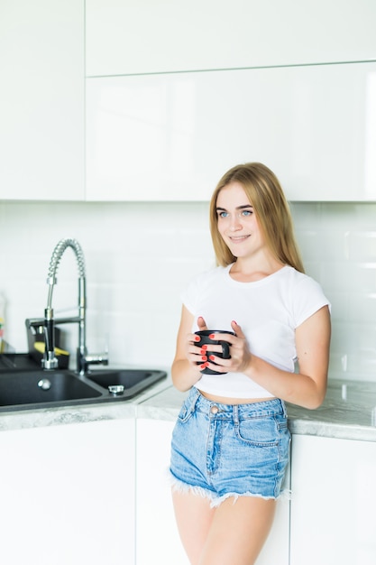 Caffè bevente della bella giovane donna felice a casa di mattina