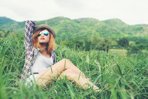 Beautiful hipster woman sitting in a meadow with nature and moun