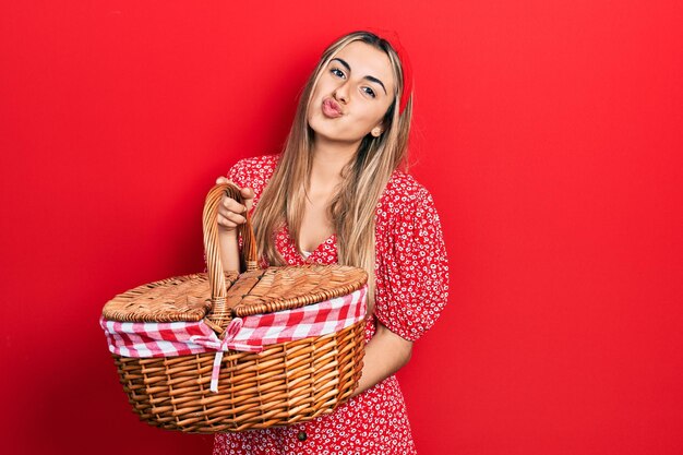 Beautiful hispanic woman holding picnic wicker basket looking at the camera blowing a kiss being lovely and sexy love expression