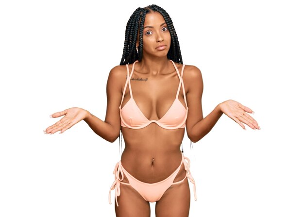 Beautiful hispanic woman wearing bikini clueless and confused expression with arms and hands raised. doubt concept.