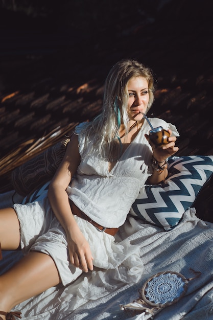 Beautiful Indian hippie girl with long blond hair on the roof drinking mate tea. 
