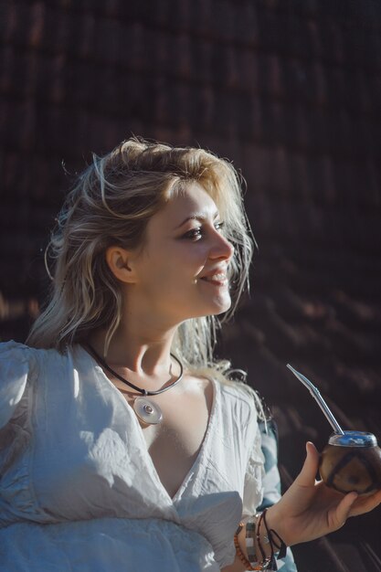 Beautiful Indian hippie girl with long blond hair on the roof drinking mate tea. 