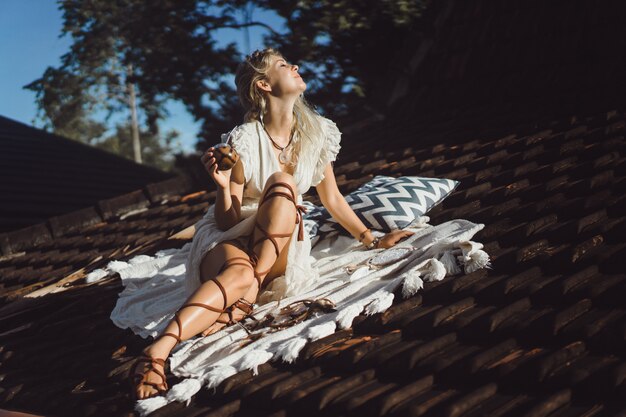 Beautiful Indian hippie girl with long blond hair on the roof drinking mate tea. 