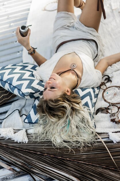 Beautiful Indian hippie girl with long blond hair on the roof drinking mate tea.