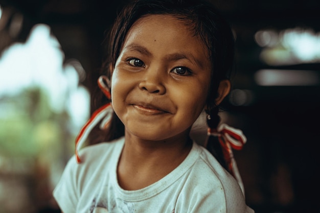 無料写真 おさげとリボンを持つ美しいインドネシアの子供の女の子。大きな黒い目を持つ美しいバリの女の子。バリ、2021年11月