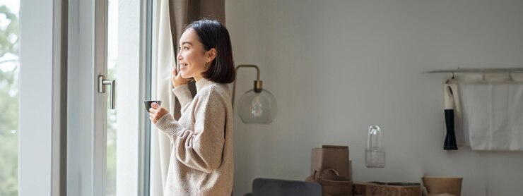 無料Photo 家にいて窓の外を見てコーヒーエスプレッソを飲みながら微笑む美しい韓国人女性