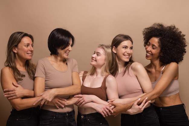 Beautiful ladies of different ages and nations in brown tops look at each other holding hands on beige background