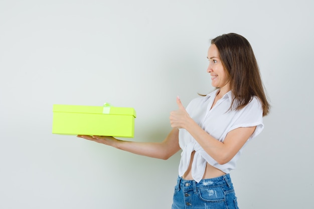 Beautiful lady giving a gift to someone while showing thumb up in white blouse,jeans front view.