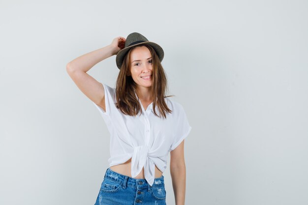 Beautiful lady holding hand on head in white blouse,hat , front view. space for text