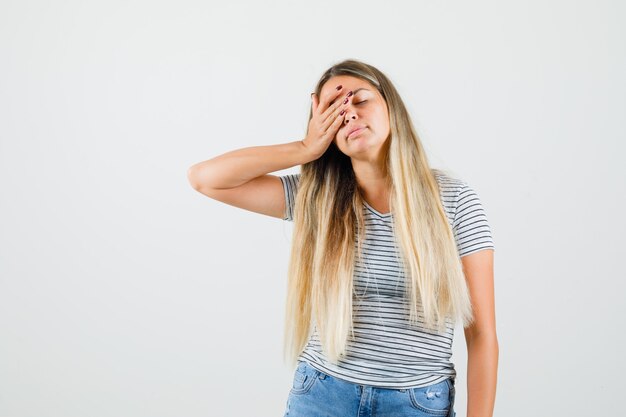 Beautiful lady holding hand on her eye in t-shirt and looking sleepy , front view.