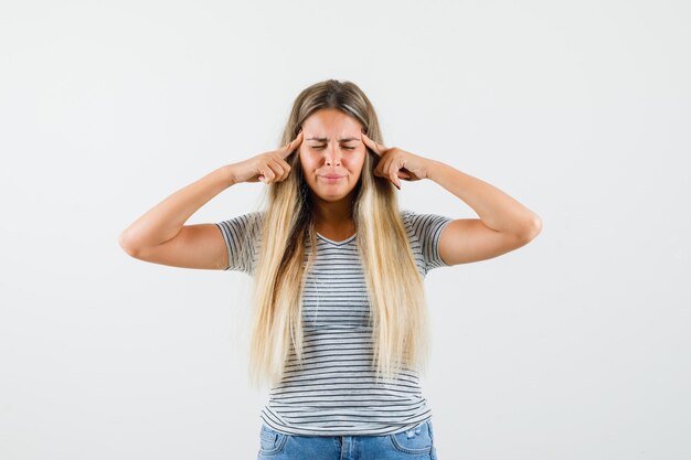 Beautiful lady holding hands on her head in t-shirt and looking painful. front view.