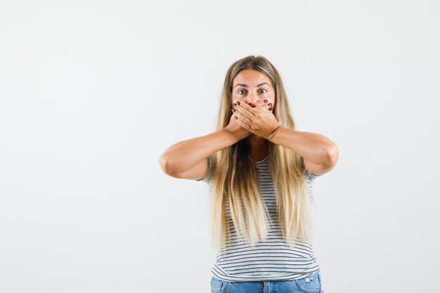 Beautiful lady holding hands on her mouth in t-shirt and looking scared. front view.