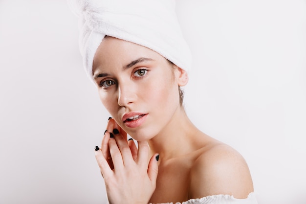 Beautiful lady is gently on white wall. Young model with clean healthy skin posing with towel .