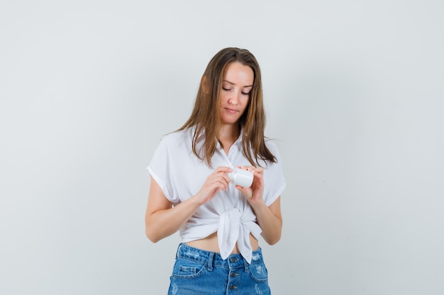 Beautiful lady looking at bottle of pills in white blouse,jeans and looking attentive , front view.