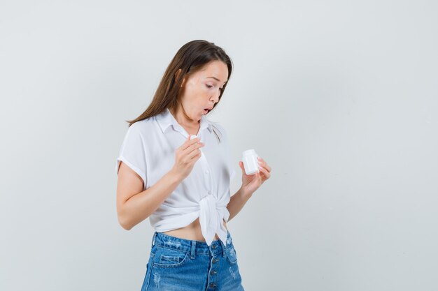 Beautiful lady looking inside of bottle in white blouse and looking surprised. front view.