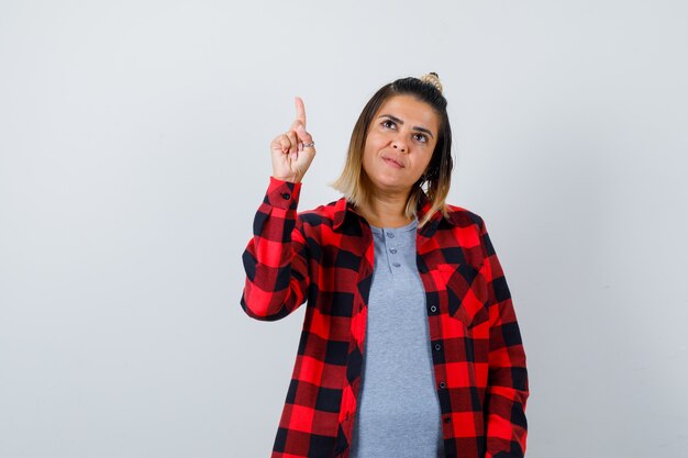 Beautiful lady pointing up, looking upward in casual clothes and looking hopeful , front view.