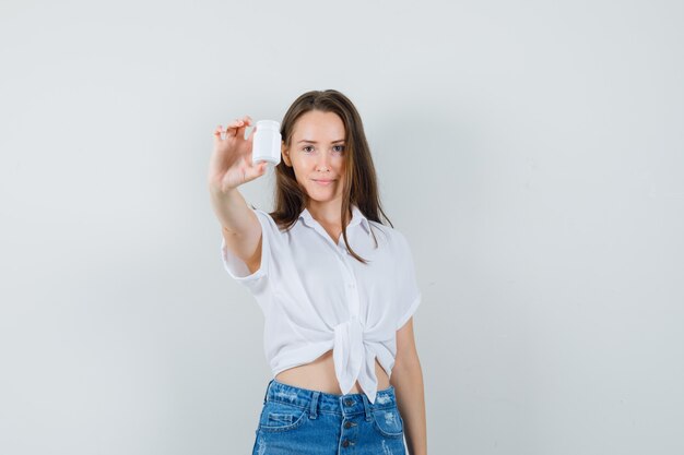 Beautiful lady showing bottle of pills in white blouse , front view.