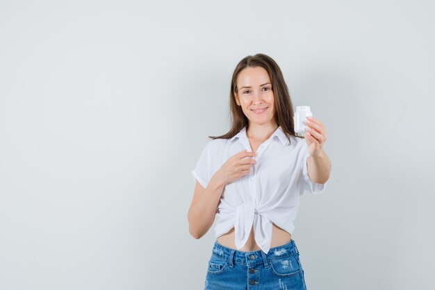 Beautiful lady showing bottle of pills in white blouse and looking pleased. front view. space for text