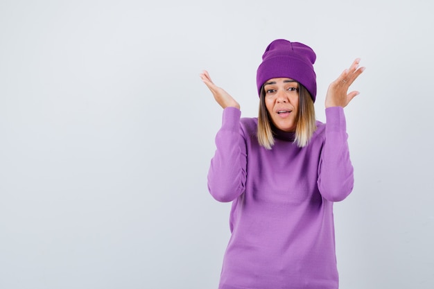 Free photo beautiful lady showing helpless gesture in sweater, beanie and looking helpless . front view.