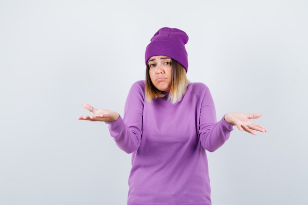 Beautiful lady showing helpless gesture in sweater, beanie and looking indecisive . front view.