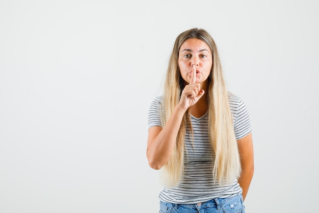 Beautiful lady showing silence gesture in t-shirt and looking focused. front view.