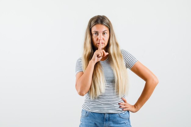 Beautiful lady showing silent gesture in t-shirt and looking serious. front view.