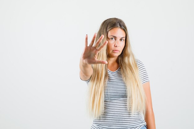 Beautiful lady showing stop gesture in t-shirt and looking serious. front view.