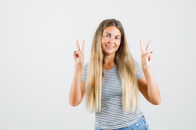 Beautiful lady showing v-sign with both hands in t-shirt and looking cheerful , front view.