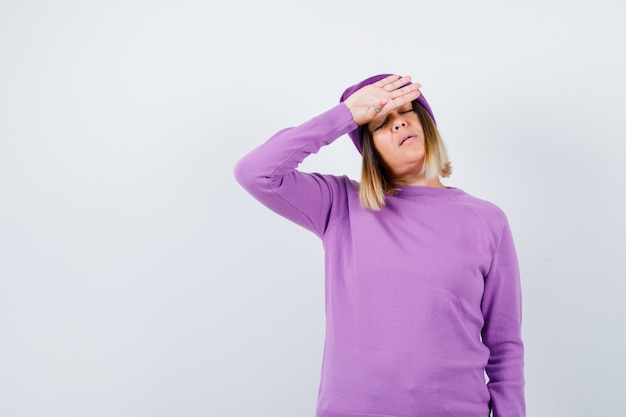 Beautiful lady in sweater, beanie keeping hand on forehead and looking weary , front view.