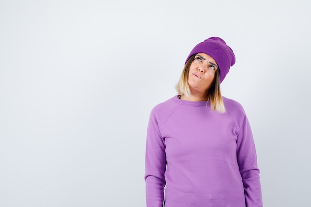 Free photo beautiful lady in sweater, beanie looking up and looking preoccupied , front view.