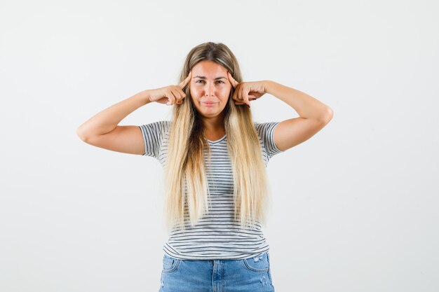 Beautiful lady in t-shirt holding hands on her head and looking painful , front view.