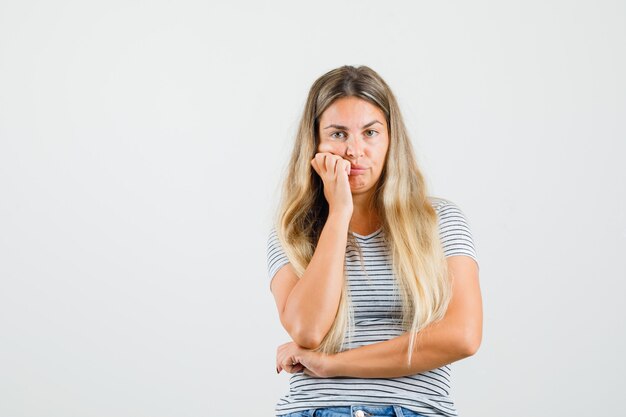 Beautiful lady in t-shirt leaning face on her cheeks and looking tired , front view.