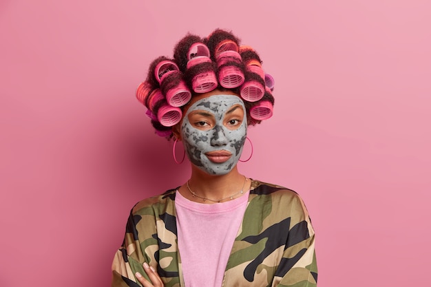 Beautiful lady wearing mask for face care wearing hair curlers isolated