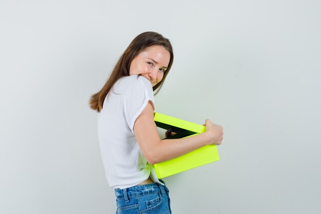 Beautiful lady in white blouse cuddling gift box and looking merry , front view.