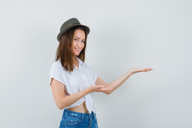 Beautiful lady in white blouse,hat spreading palms aside and looking cheery , front view.