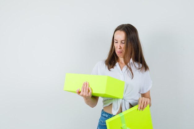 Beautiful lady in white blouse,jeans looking inside yellow box , front view.