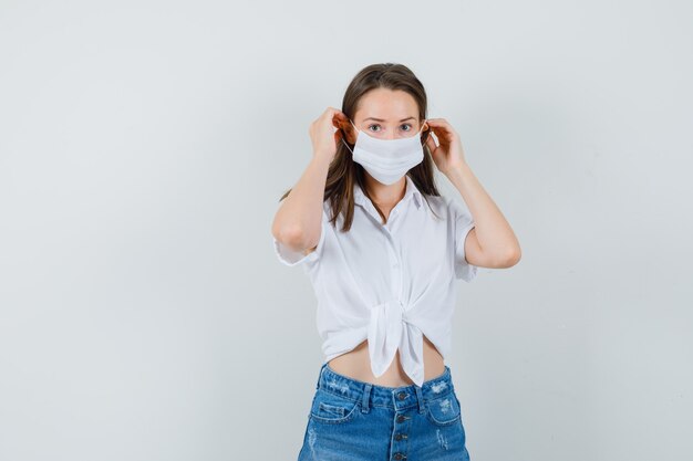 Beautiful lady in white blouse,jeans wearing face mask , front view.