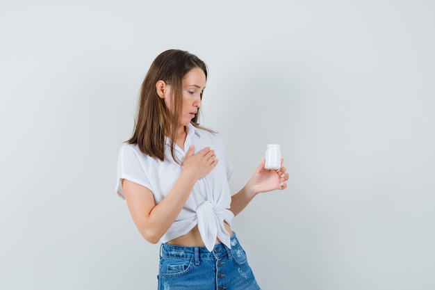 Beautiful lady in white blouse looking at bottle of pills and looking focused , front view.